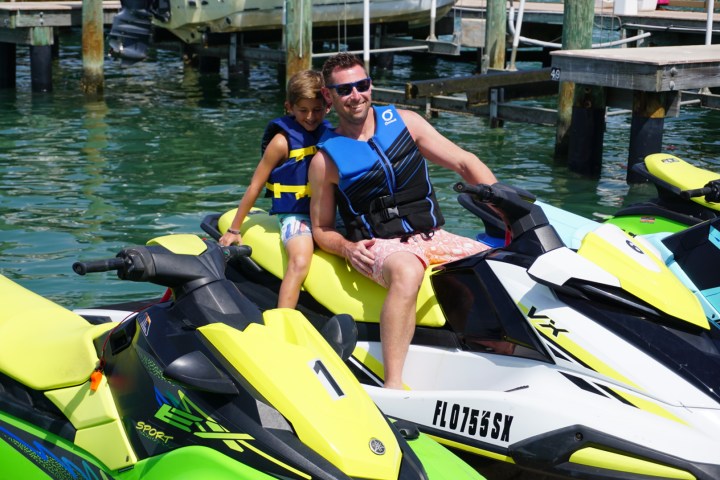 Dad and son in life jackets sitting on a jet ski parked at the dock